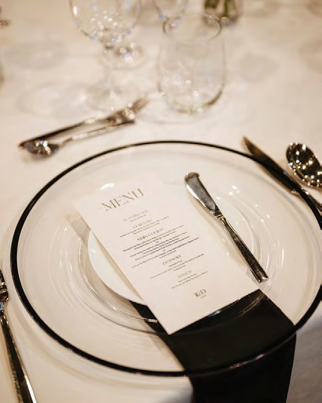 Formal dining place setting with stacked plates, knife, and spoon, and a menu card on a black napkin in front of the plate.