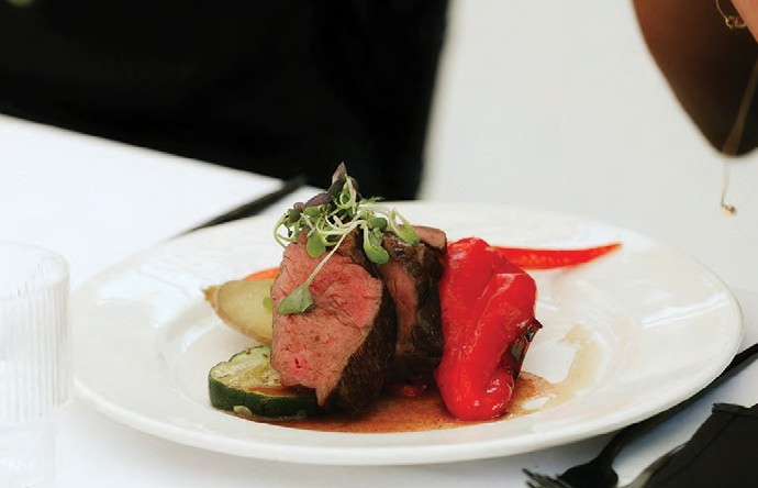 Plate with medium-rare steak slices, zucchini, red pepper, and sauce garnished with microgreens on a white plate.