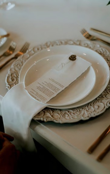 Formal dining table setting with a folded white napkin and menu on a decorative plate at center of table.