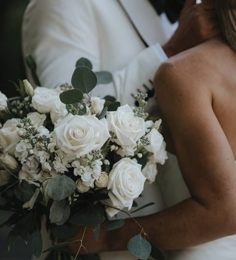 Bride holding a white rose bouquet with greenery, close to her shoulder.