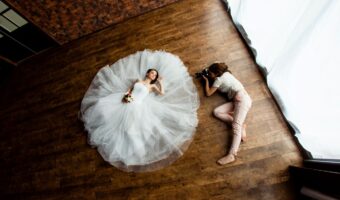 bride laying on wood floor with train spread out in a circle while wedding photographer taking portrait