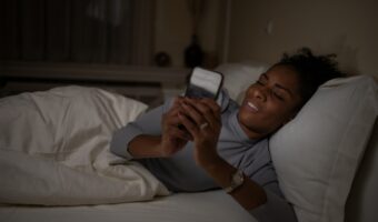 Woman lying in bed at night, smiling while looking at her smartphone.