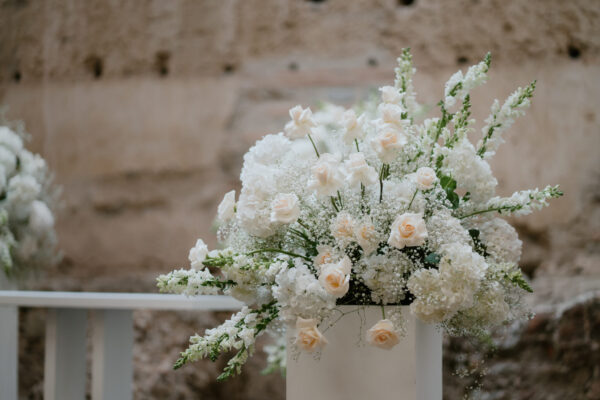 Elegant white floral arrangement with pale peach roses and baby's breath resting on a white stand outdoors