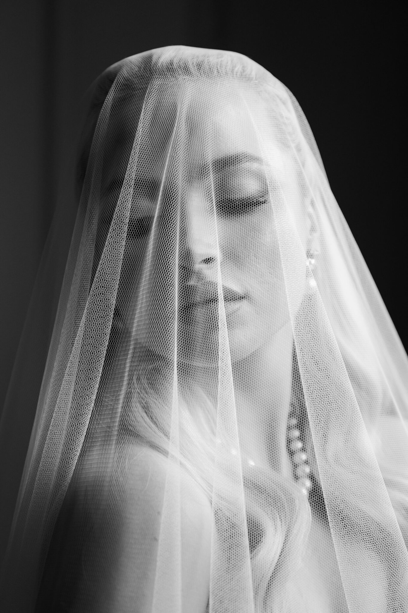Bride-like portrait with a sheer veil draped over the face in black and white.