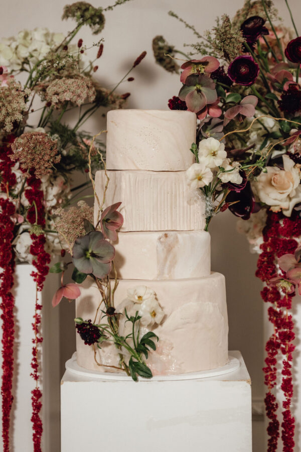 Three-tier marble-pink wedding cake with delicate blush flowers and greenery cascading around it.