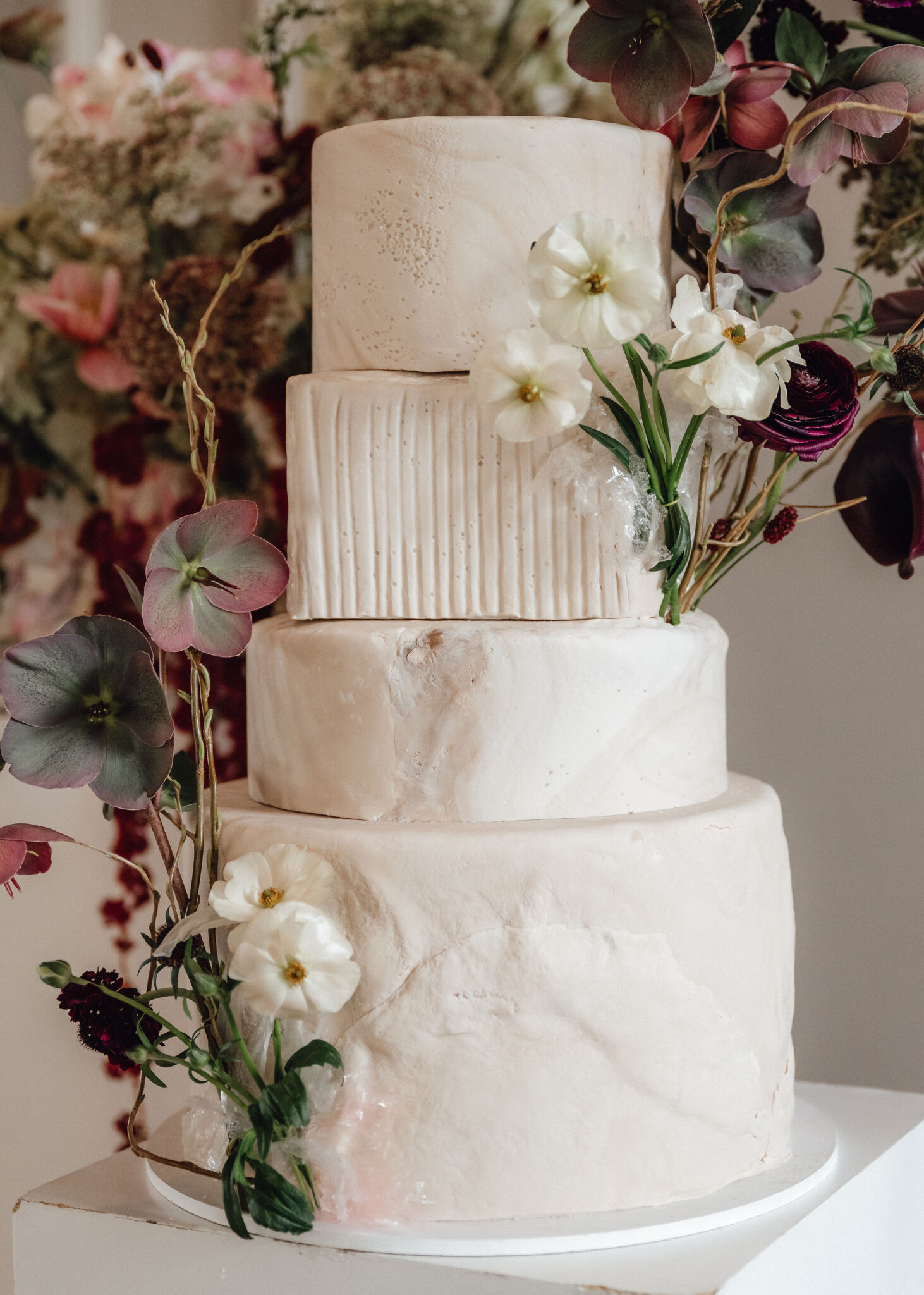 Three-tier white wedding cake with textured sides and a cascading arrangement of white flowers and greenery around the top and middle tiers.