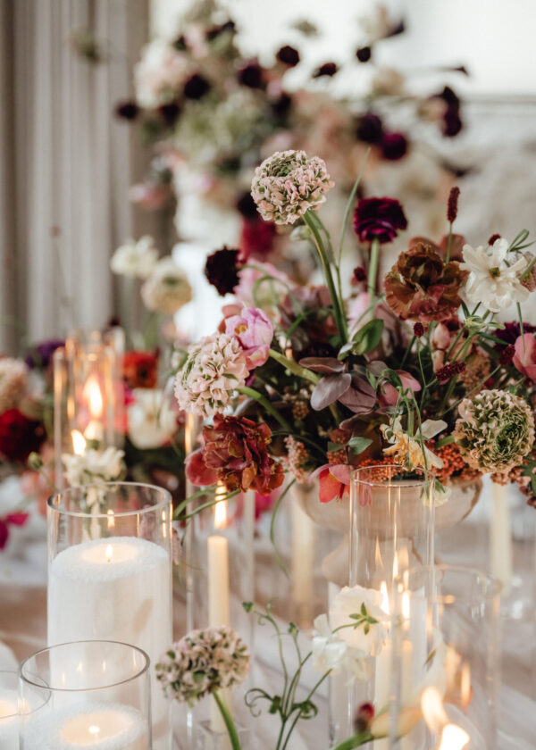 Elegant table centerpiece with pink and cream flowers and tall glass candle holders amid soft candlelight.