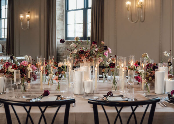 Elegant banquet table with tall floral centerpieces, candles in glass holders, and place settings in a softly lit room.