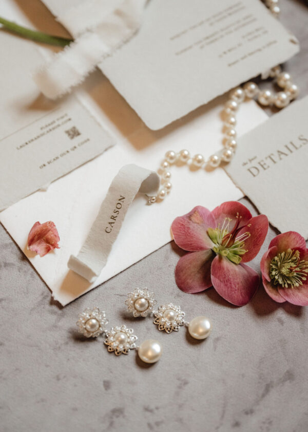 Pearl jewelry laid on white cards with pink flowers, including a pearl bracelet and cluster earrings.