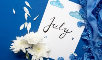 White card with the word July written in cursive on a blue background, adorned with white chrysanthemums, petals, and blue lace.