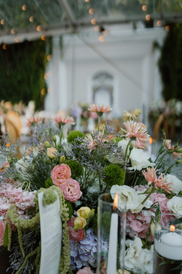 Close-up of pastel flower centerpiece with pink roses, lavender, and white blooms at a candlelit event table.