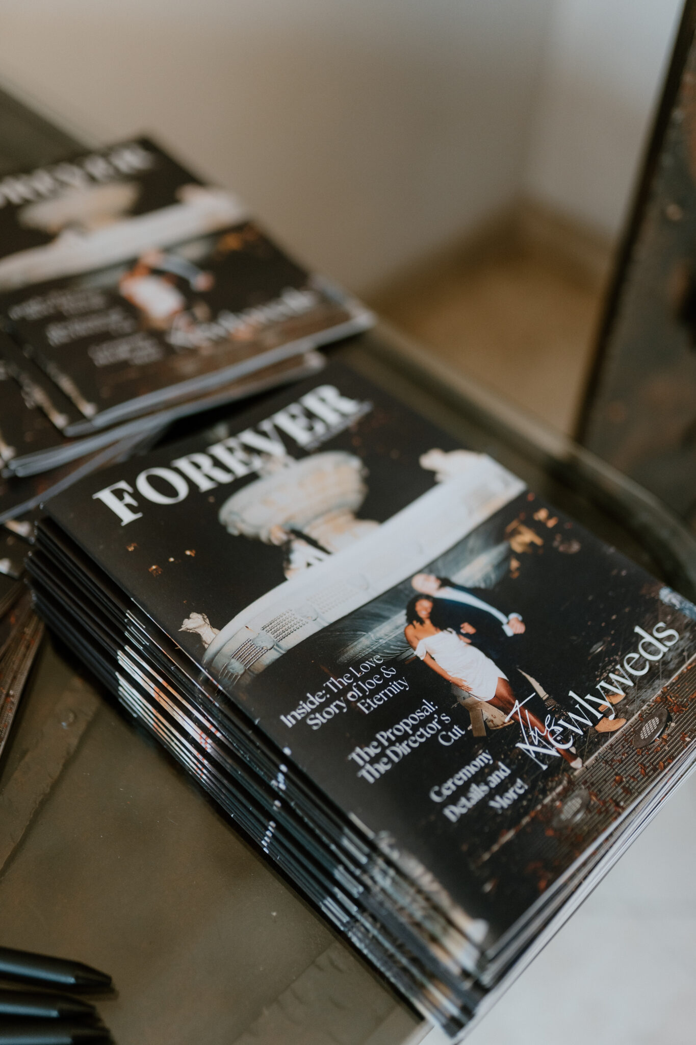 Stack of glossy magazines on a table, the top issue showing the word 'FOREVER' on its cover.
