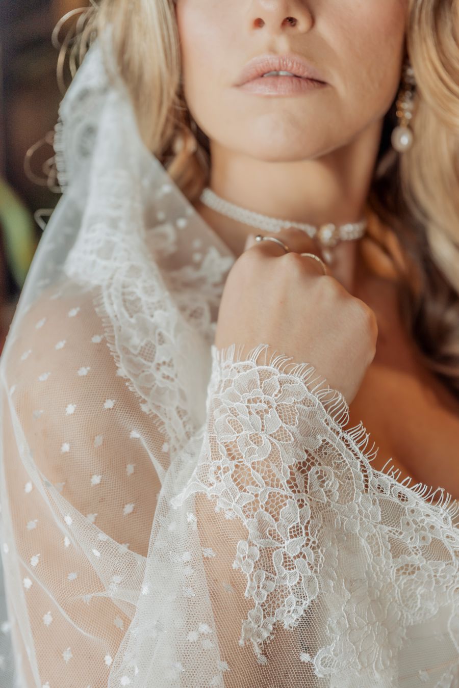 Close-up of a woman wearing a lace wedding veil and pearl jewelry, resting her chin on her hand.