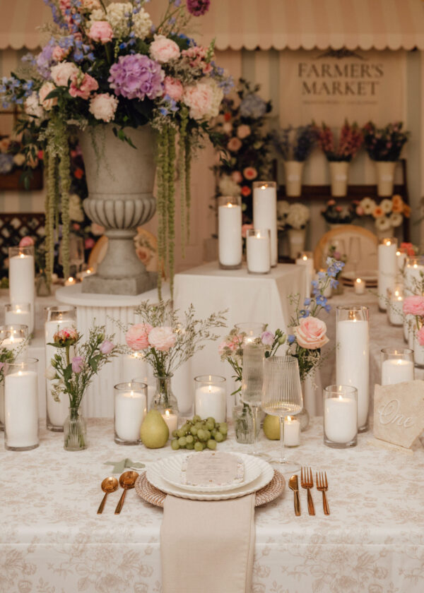 Elegant wedding reception table with a tall floral centerpiece in a gray urn, white candles, and gold flatware.