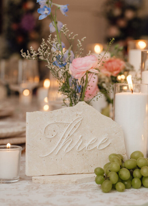 Stone centerpiece with pink flower and white blossoms, carved cursive writing, candlelight and a bunch of green grapes (wedding table decor).