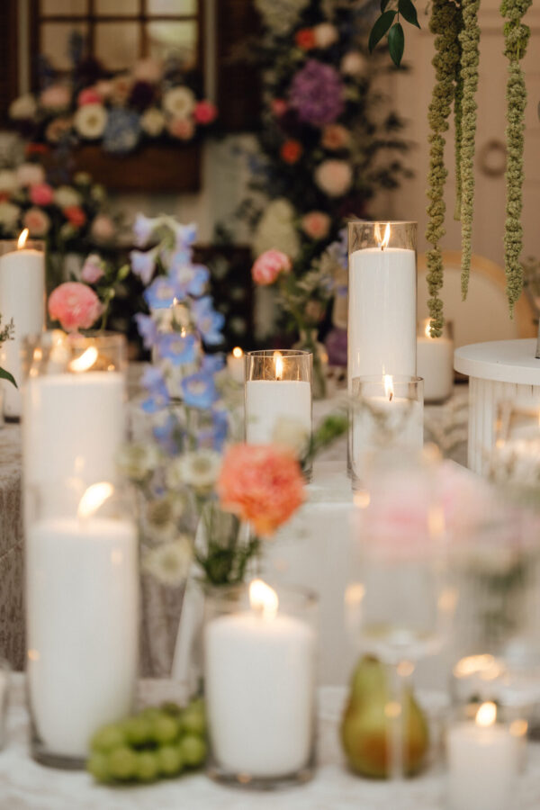 Candlelit wedding table centerpiece with tall white pillar candles and soft-flowered backdrop (blurry).