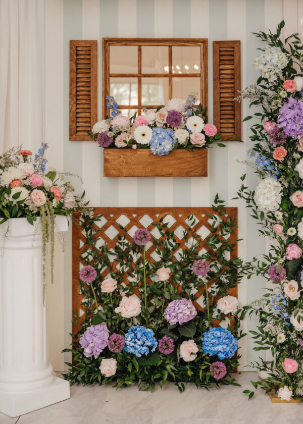 Wooden window frame with pastel flower arrangement and greenery, set against striped wall in an elegant decor display.