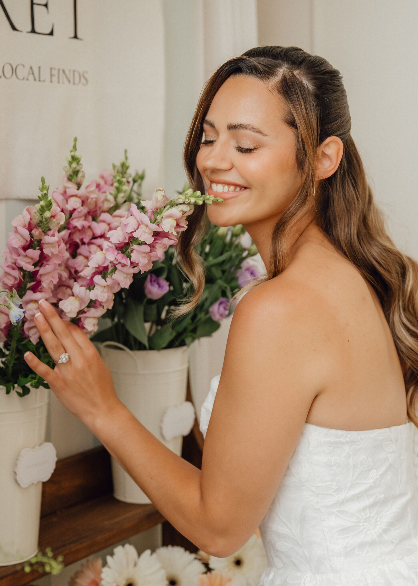 Woman in a white dress smelling a bouquet of pink flowers in a shop window display