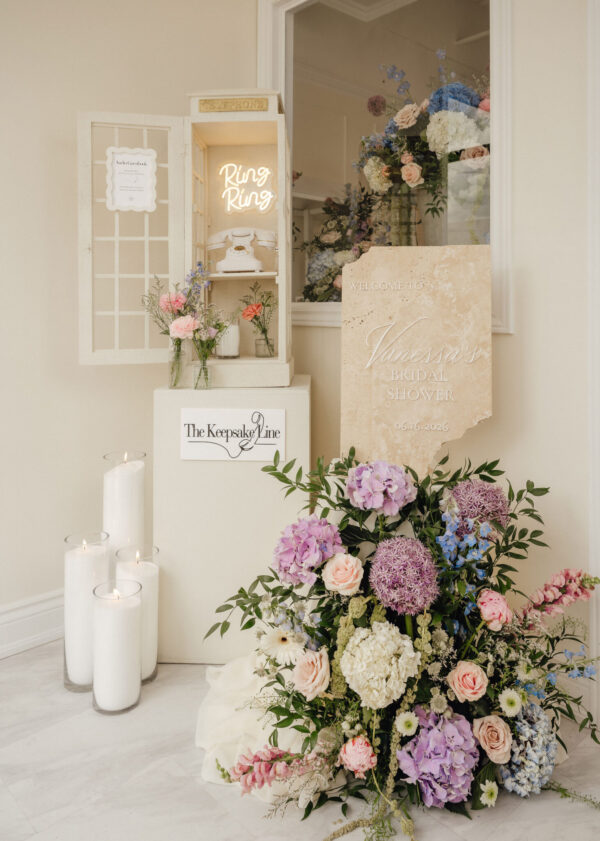 Bridal shower floral arrangement with pink, blue, and purple blooms beside a cream display and candles.