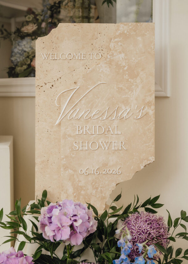 Stone sign reading 'Welcome to Vanessa's Bridal Shower' with date 06.16.2026, framed by pink and purple flowers.