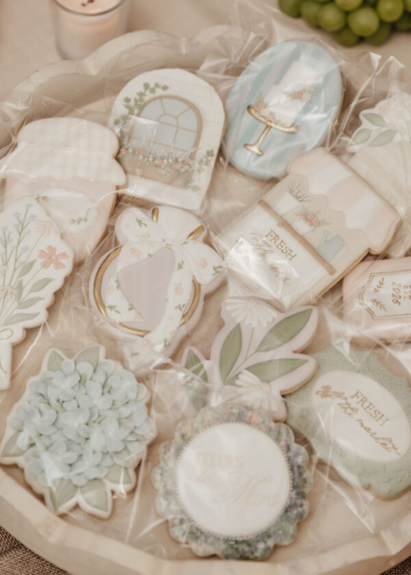 Assorted pastel decorated cookies in heart, flower, and cake-table shapes, arranged in a clear cellophane bag for gifting.