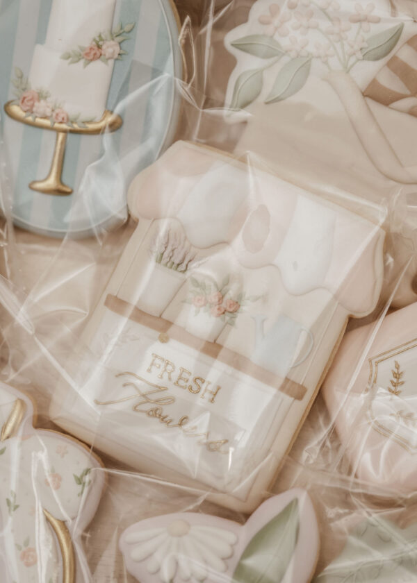 Pastel wedding-themed cookies and decorations with floral icing in soft blue, pink, and cream, wrapped in plastic.