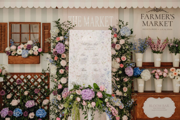Pastel flower display and signage for 'The Market' with wedding seating chart in front of a floral backdrop