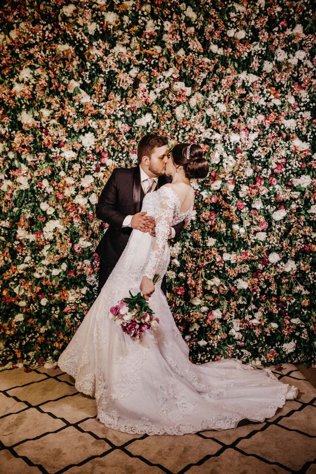 bride and groom kiss in front of flower wall