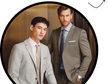 Two men in tailored suits pose for the camera in an elevator, looking confident and professional.