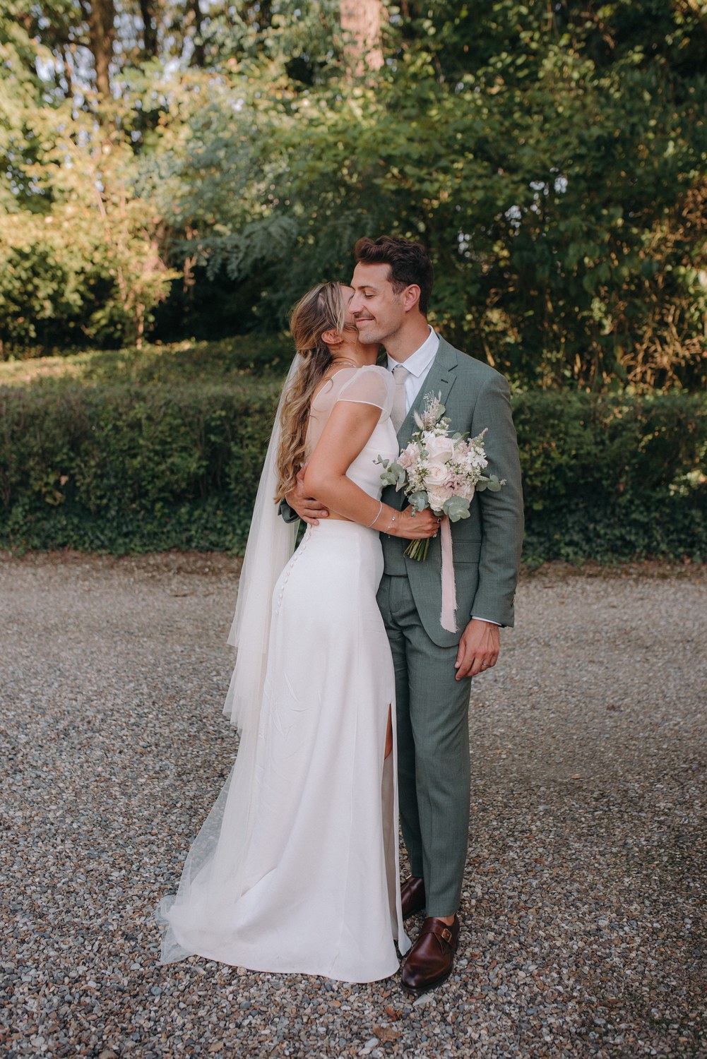 Groom in a sage green made-to-measure suit with his bride at a garden wedding