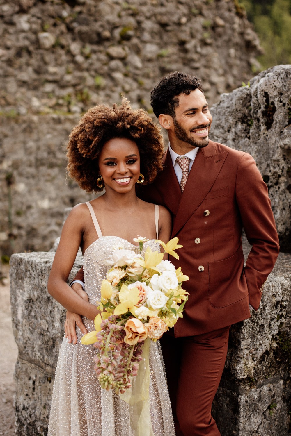 Groom in a terracotta double-breasted wedding suit with his bride at a stone ruin